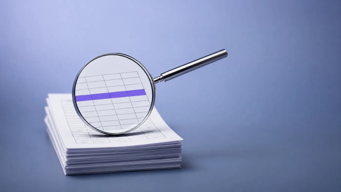 A magnifying glass held over a ruled ledger page with one row picked out, representing Vigor's audit and assurance services in Dubai